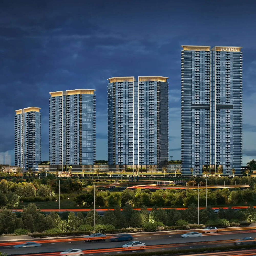 Five tall, modern residential towers with illuminated rooftops stand against a dusky sky, surrounded by greenery and a busy highway—an ideal showcase of Dubai Real Estate for those seeking premium flats in Dubai.