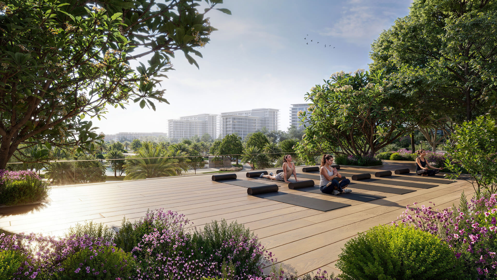Three people practice yoga on mats on a wooden deck surrounded by lush greenery and flowers, with modern buildings and palm trees in the distance—showcasing the serene lifestyle offered by premium flats in Dubai under a clear blue sky.